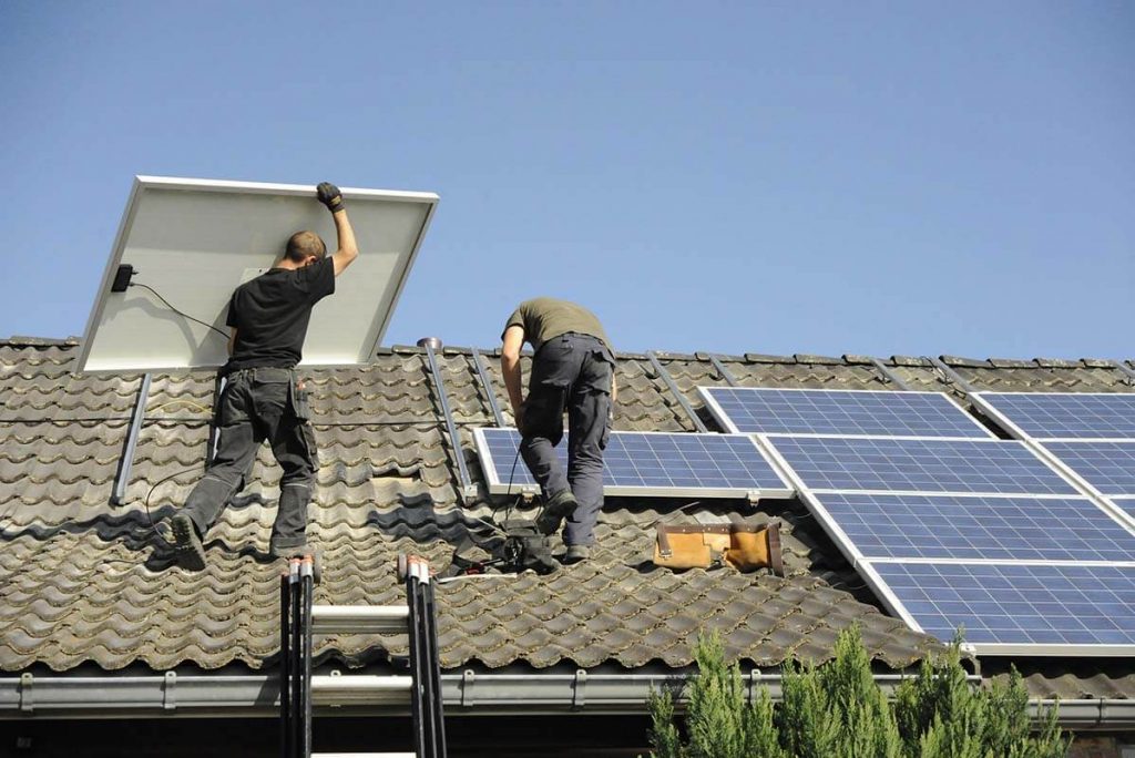 两名男子在一幢建筑物的屋顶上安装太阳能电池板